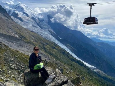 A woman on a mountainside with a cable car moving past in the background.