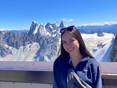 A woman poses for a photo in front of a snowcapped mountain.