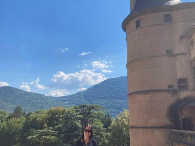 A woman poses for a photo in front of a medieval castle.