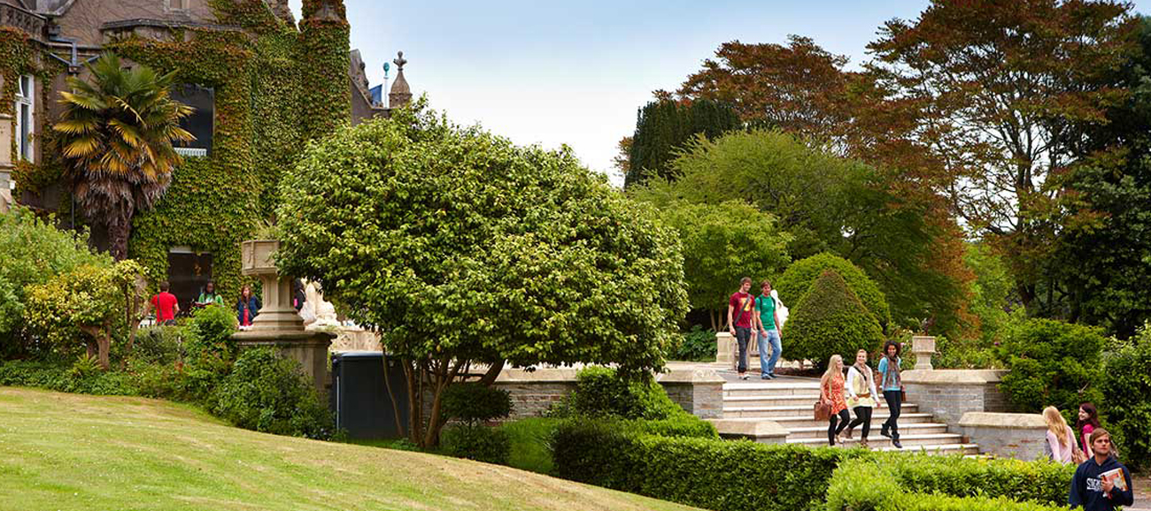 A concrete staircase in front of an ivy-covered university building surrounded by green trees and lawn at Swansea University.