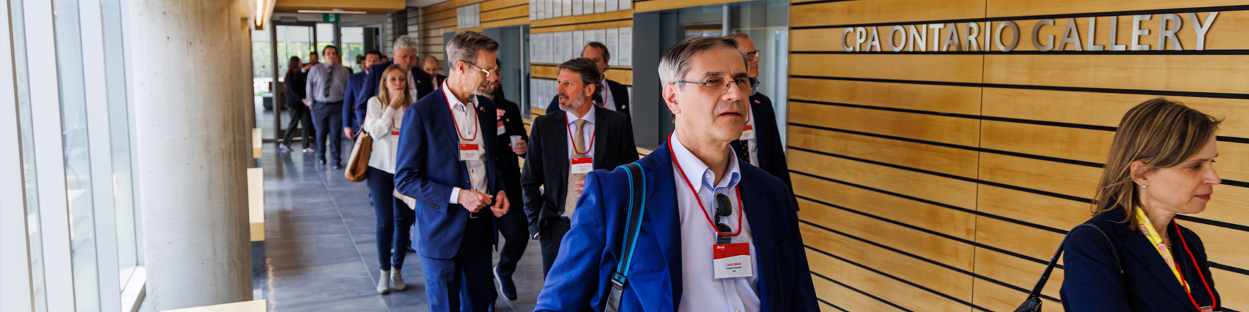 A group of people in business suits walk down a hallway casually chatting.