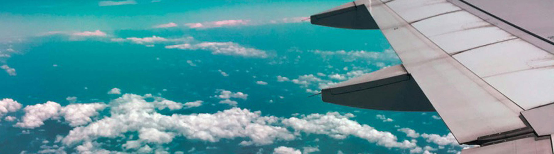 The wing of an airplane against a blue sky with clouds.