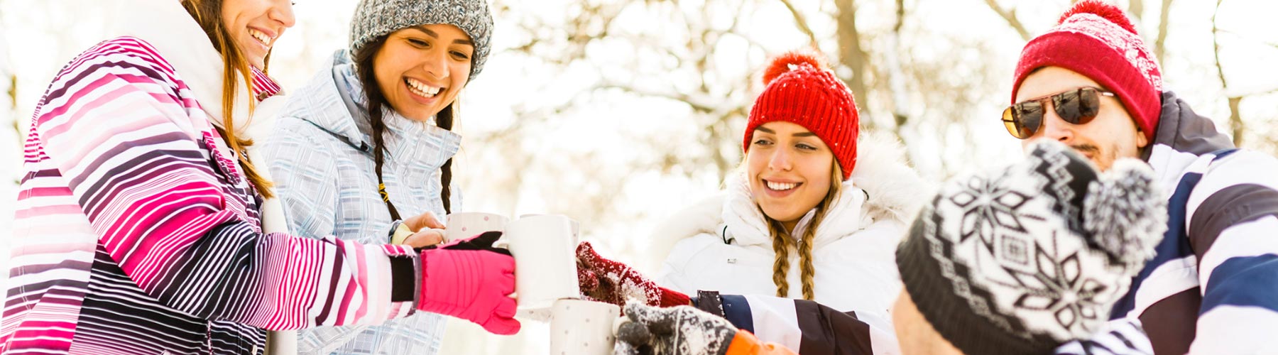 A group of people clink cups of hot beverages outside in snowy weather.