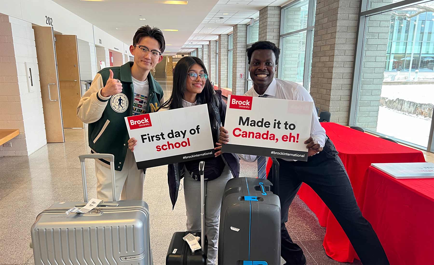 Three university students pose with suitcase and signs celebrating their first day of school in Canada. 