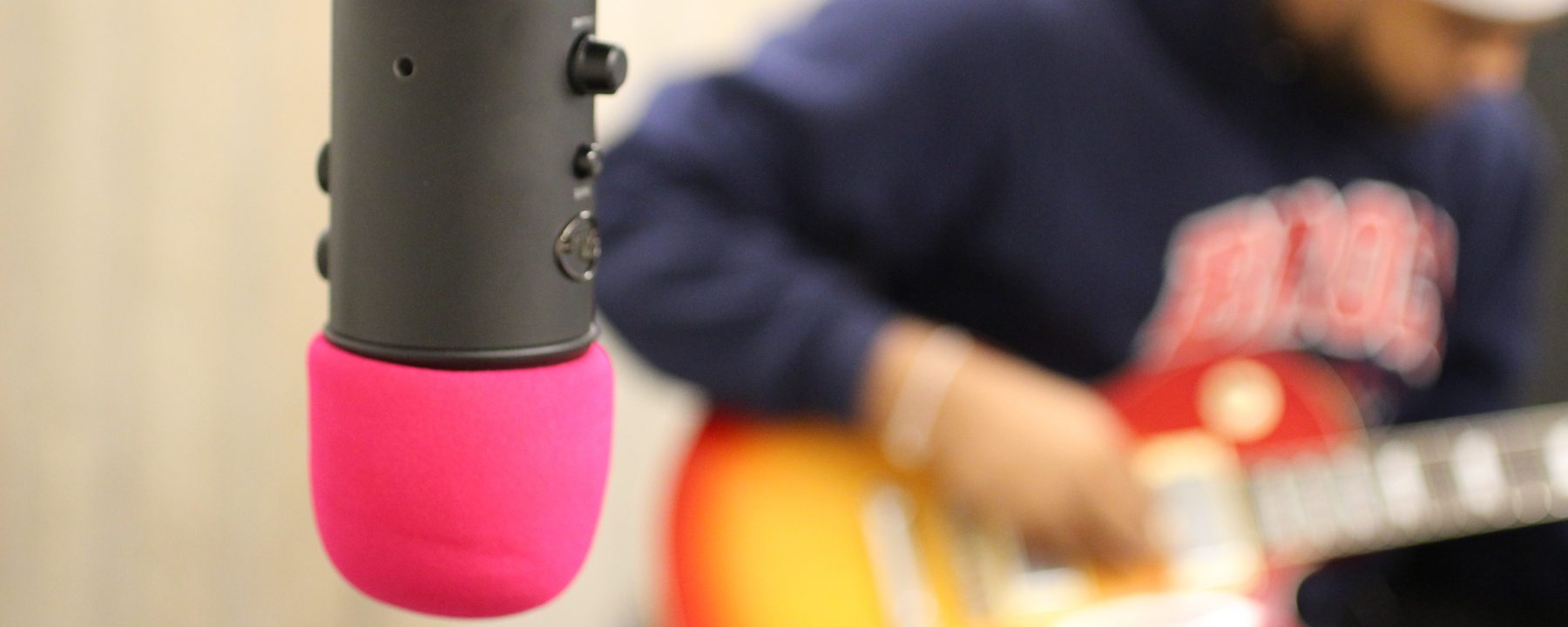 close up shot of a black and pink microphone with a person playing guitar in the back