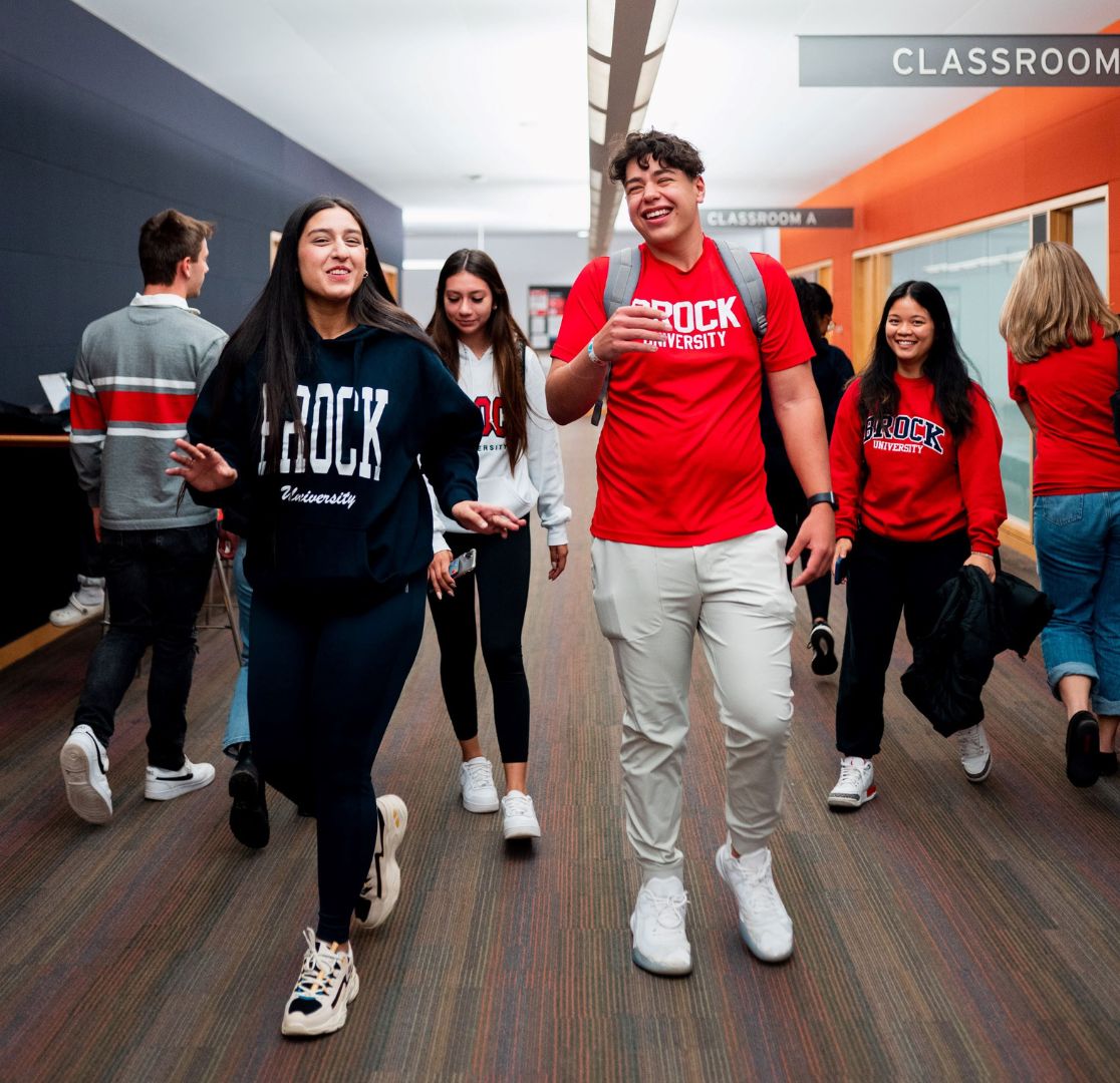 Students in Brock tshirts walk along a hallway in the Learning Commons
