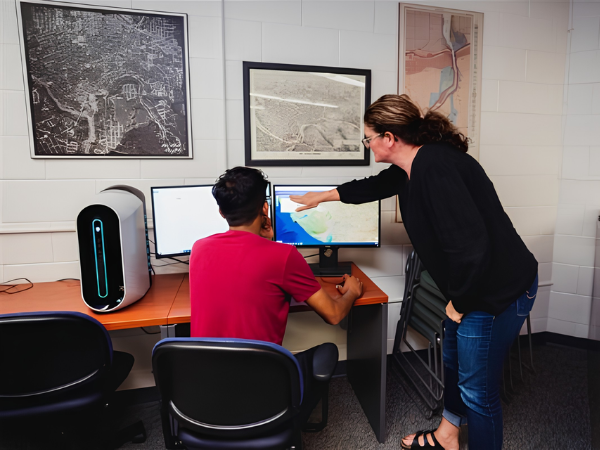 A person assists a student at a workstation in the Map, Data, GIS Library at Brock University