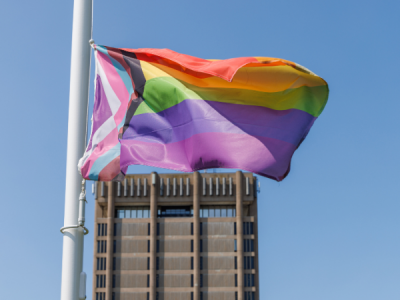 The Brock University Pride flag flies with the Schmon Tower behind it.