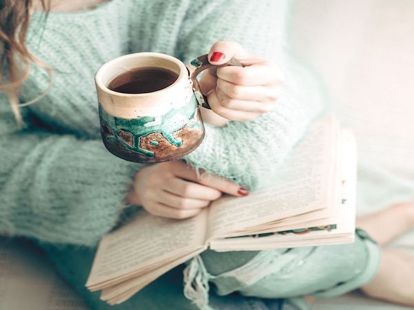 Image of a woman reading with a cup of tea in her hand