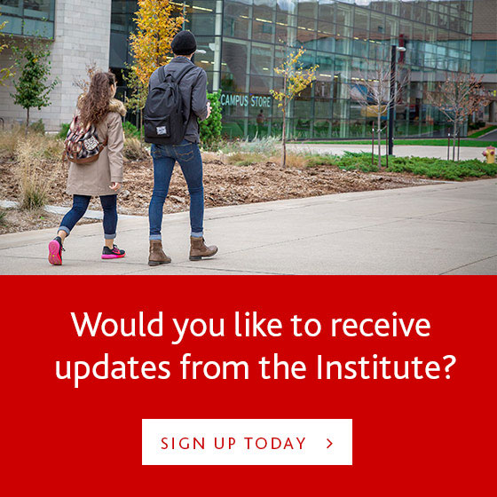 A young man and woman walk on a college campus. In the background is a glass and brick building with a sign reading "Campus Store" Underneath, a red banner with white text "would you like to receive updates from the Institute?"