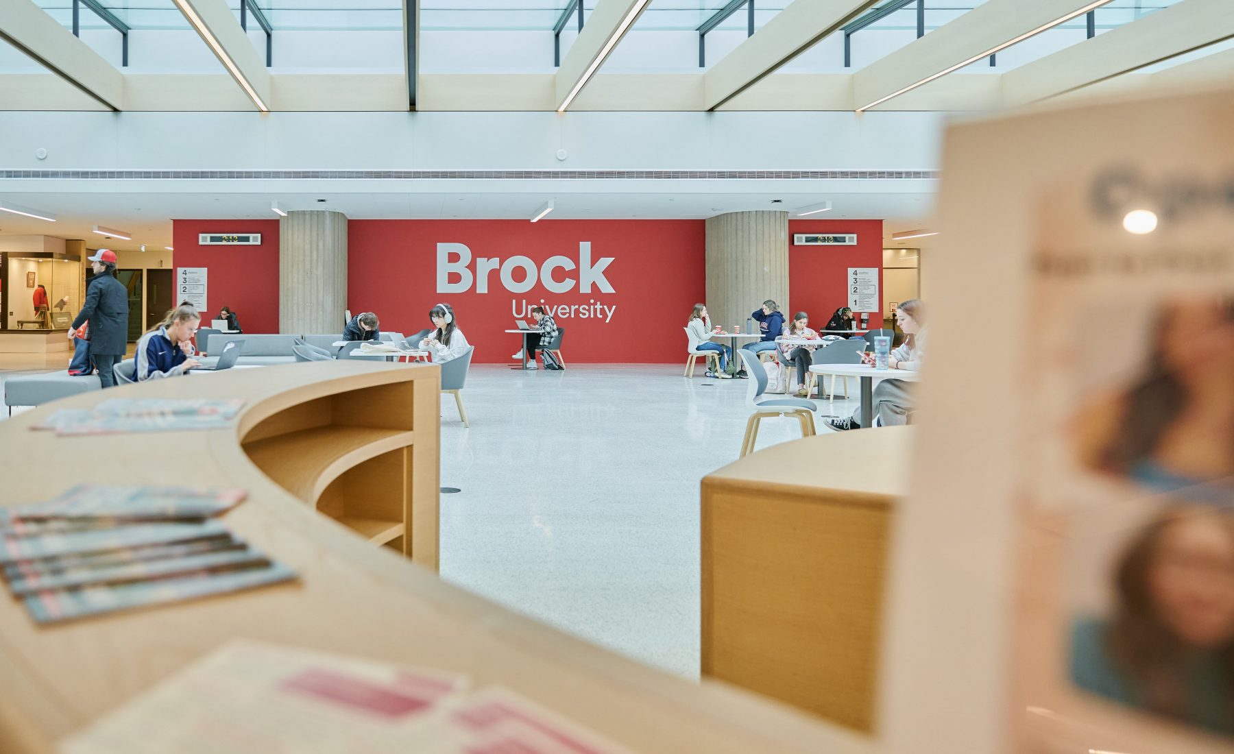 Inside view of Brock University common area with students sitting wearing earphones 