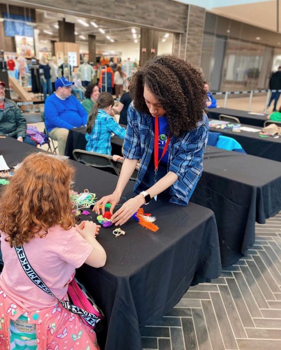 A Let's Talk Science volunteer assists a child in an activity at a community visit