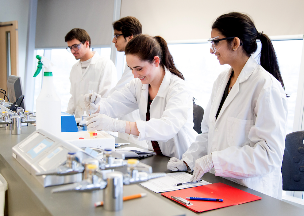 Four students in lab coats using lab equipment 