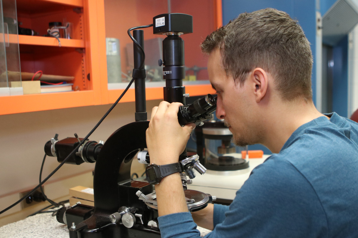 A student looks through a microscope as part of their research. 