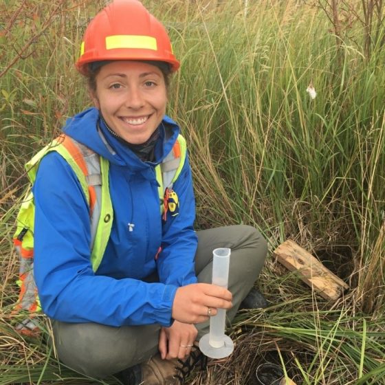 Kelly Biagi wearing saftey gear and holding a test tube among marshland