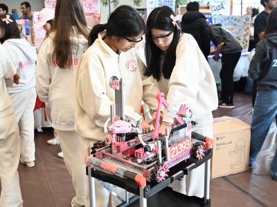 Two white uniformed women scientist students adjusting their custom robot
