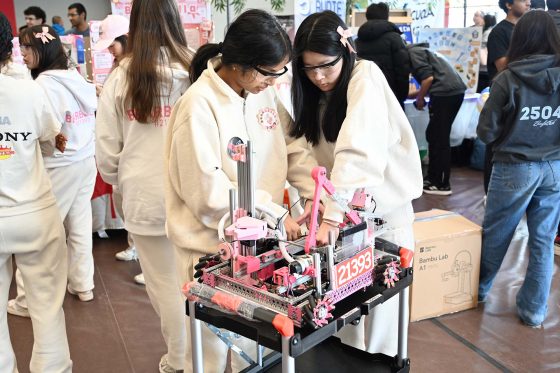 Two white uniformed women scientist students adjusting their custom robot