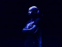 A performer stands on a stage under dark, blue light.