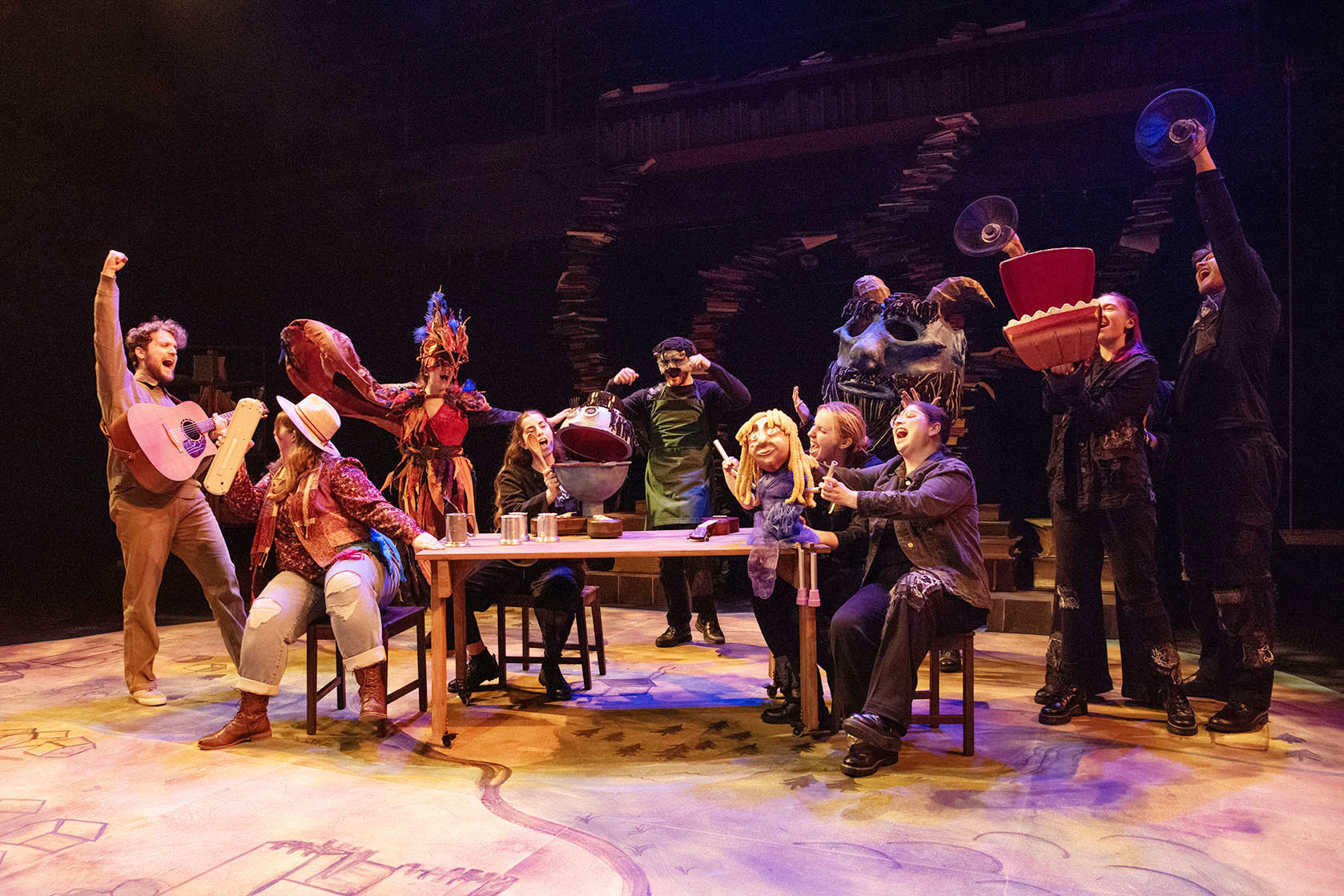 Escape to Ilkanor A group of students perform on stage sitting around a table singing.
