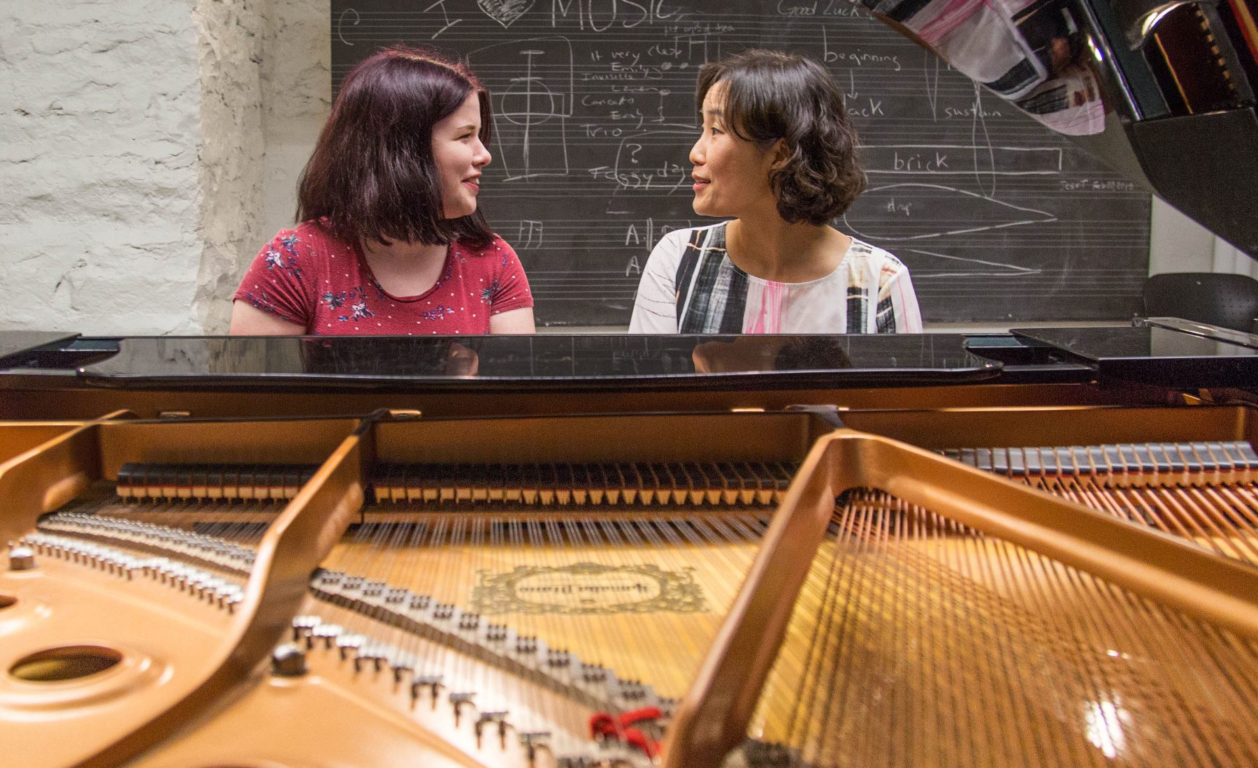Two music students sit around a piano. 