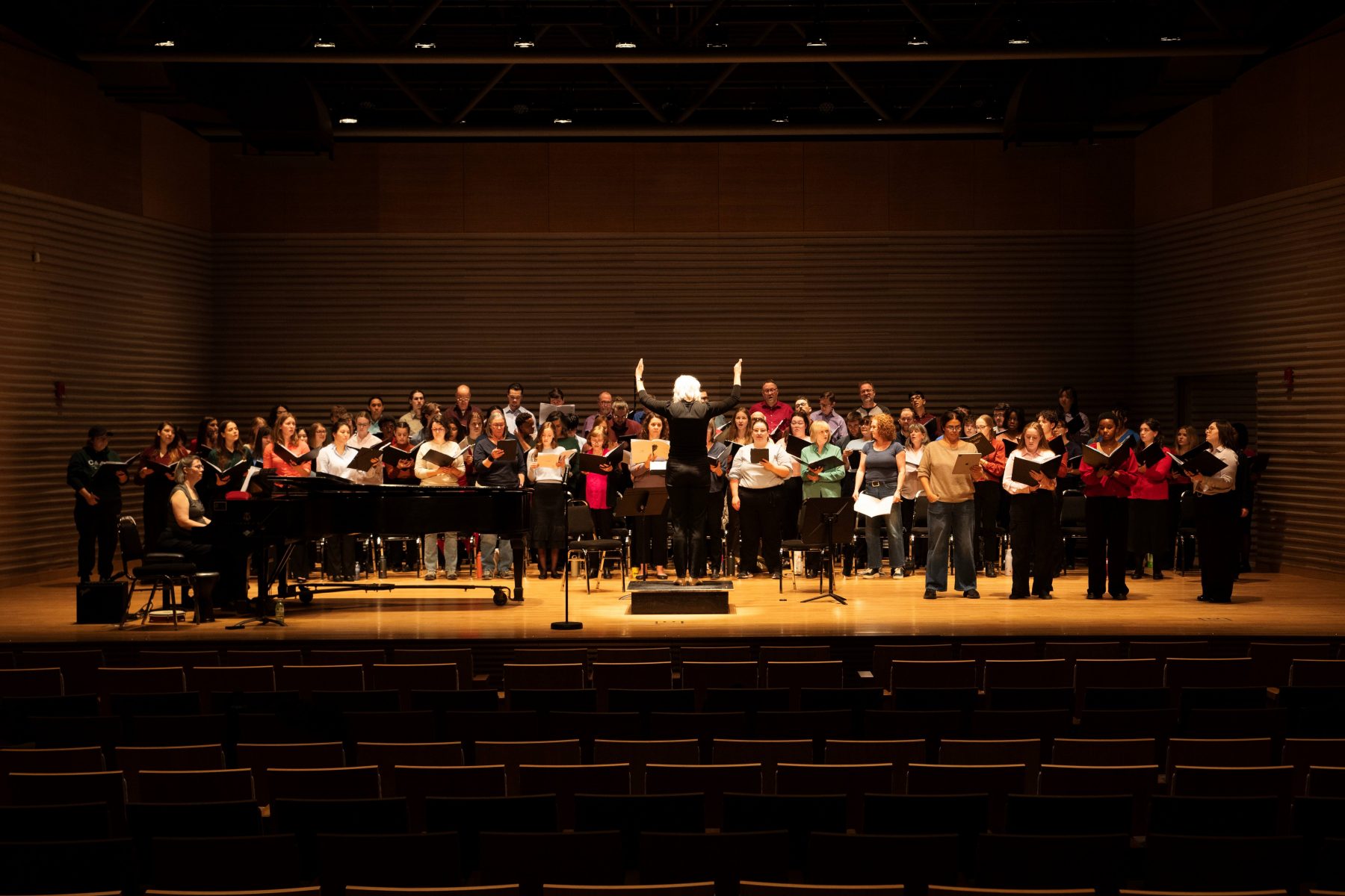 Photo of choir singing on stage with conductor seen from the back.