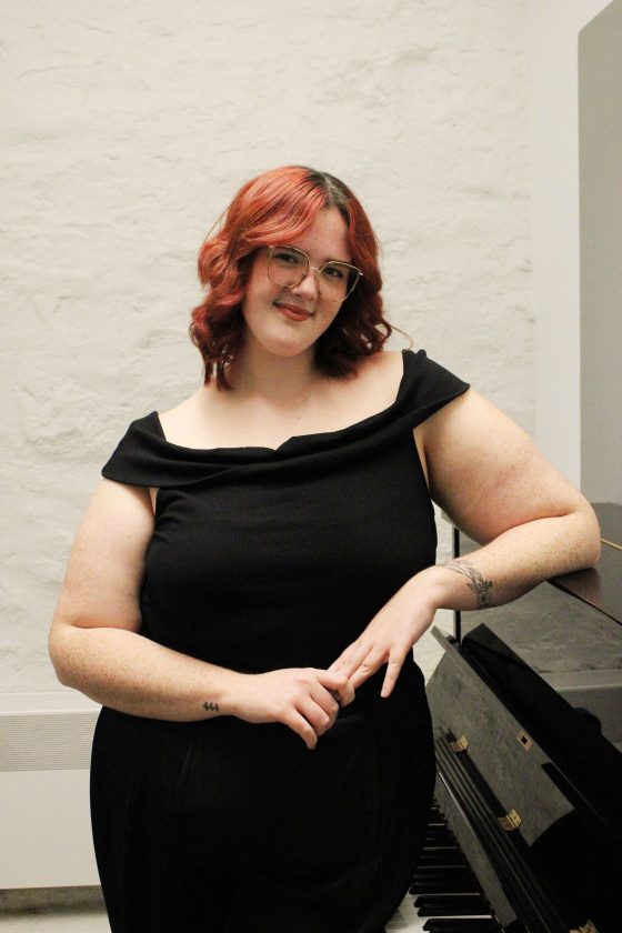 A student leans against a piano smiling.