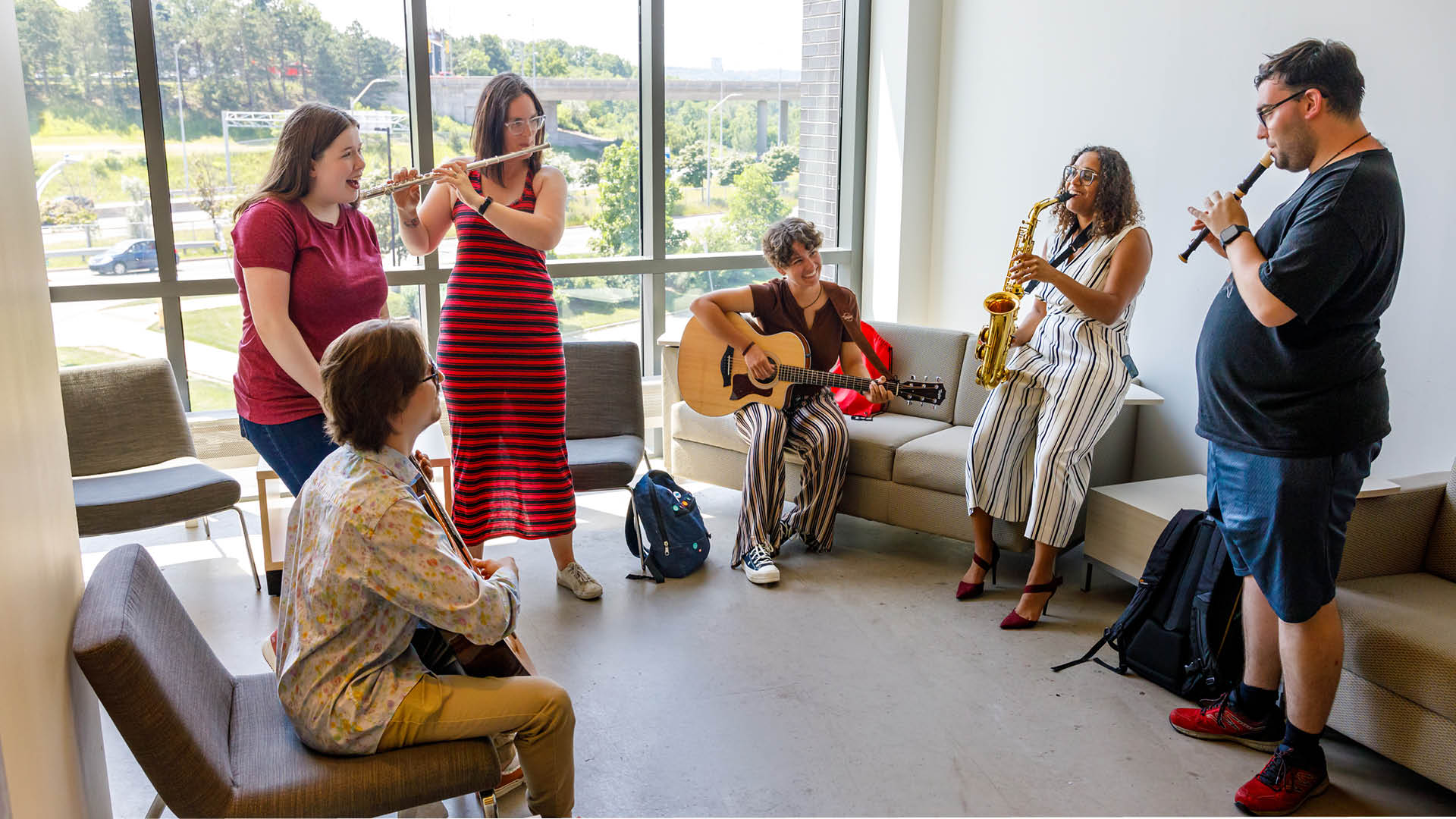 A group of students play instruments together in a brightly lit hallway. 