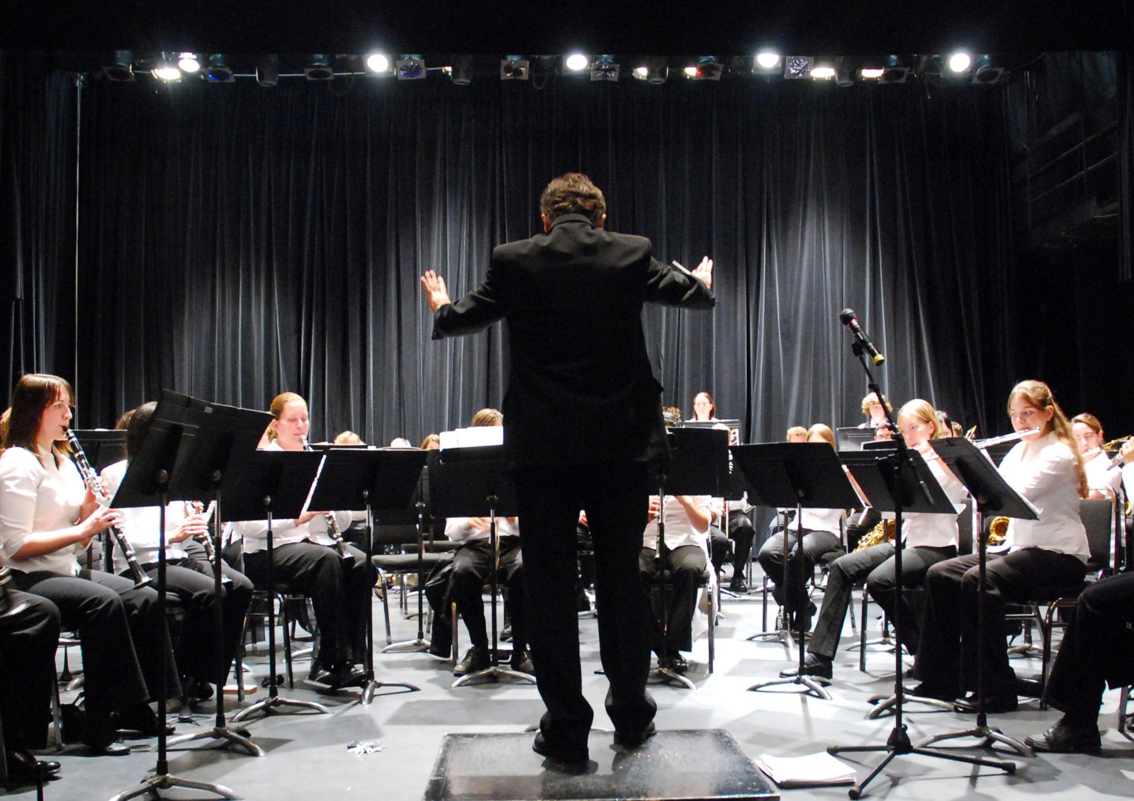 A conductor is onstage leading a group of performers.