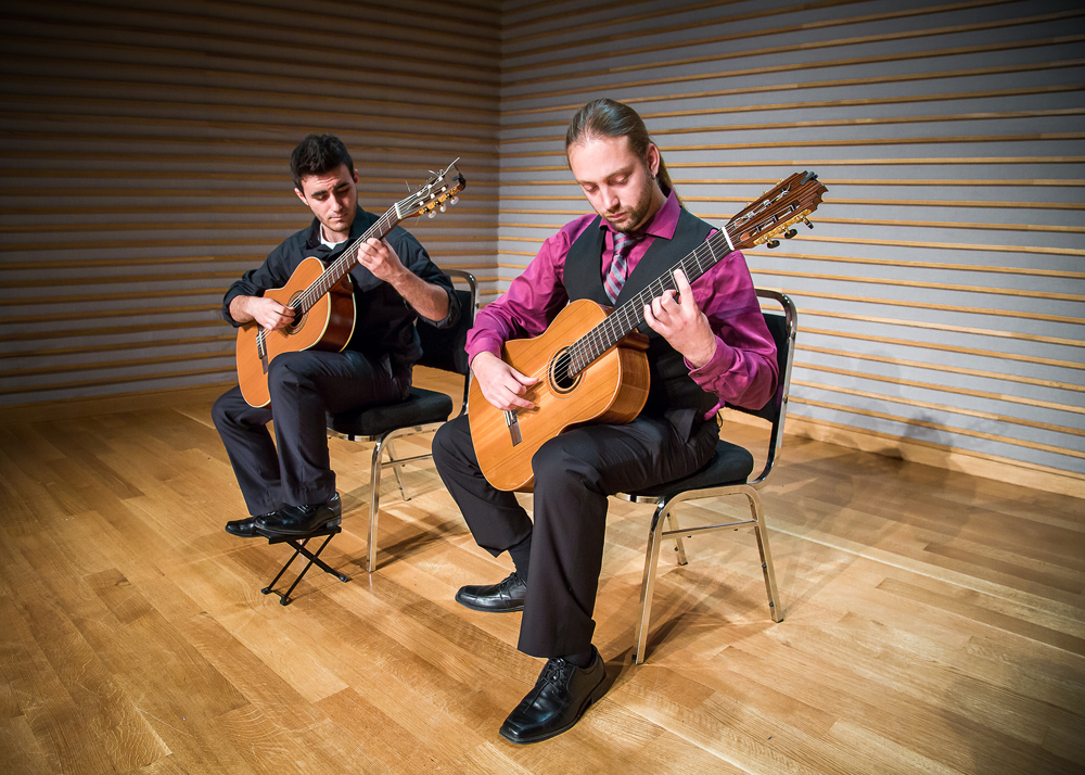 2 guitarists sitting in chairs playing