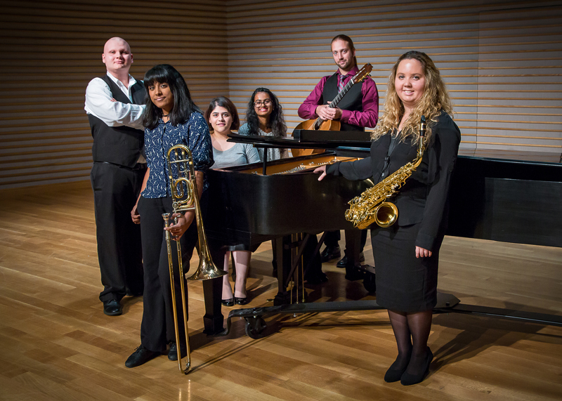 6 musicians standing by piano holding instruments
