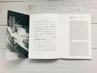 Open booklet spread featuring a black and white photo of a scaffolding structure, a handwritten musical score titled 