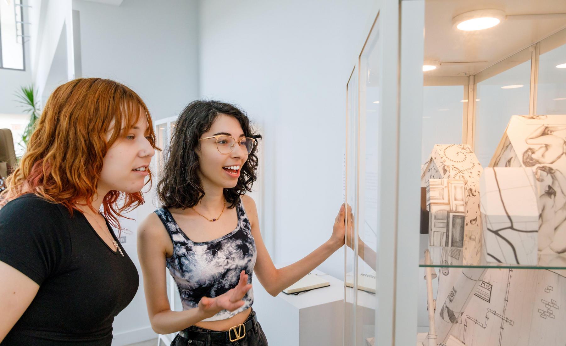 Two students observe an exhibit made of paper in the Museum in the Hallway 