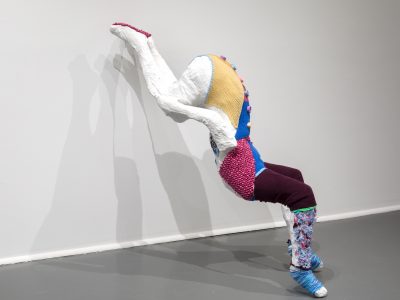 abstract sculpture of a colourful figure leaning on a white wall
