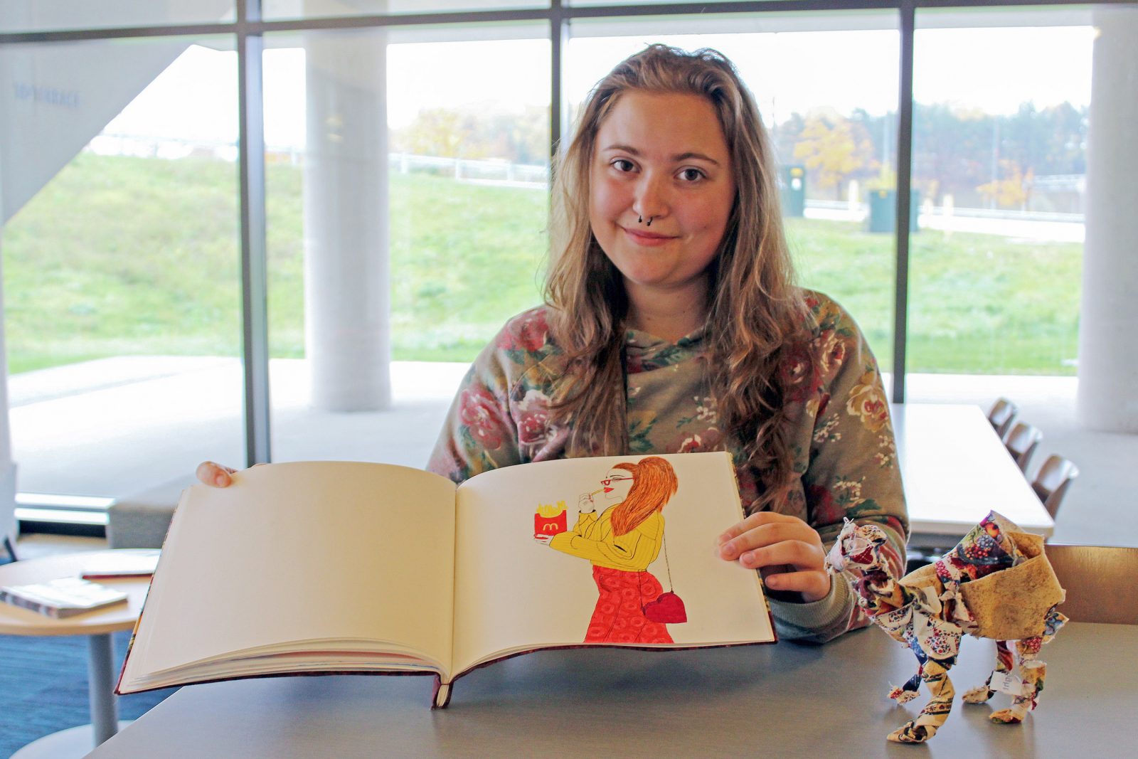 Emma Mary Sked poses with her art book and small toy animal made out of colourful fabrics.
