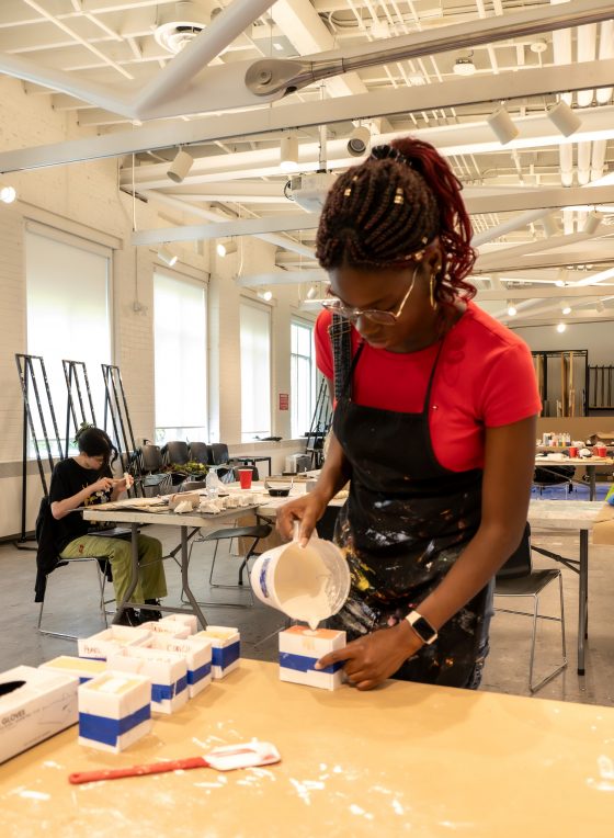 Student pours putty into molds for sculpture class.