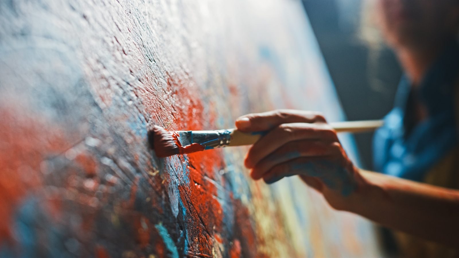 Close-up photo of a hand holding a paintbrush to a canvas