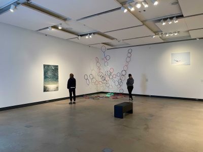 2 gallery viewers in front of art instalation of painting and large coloured hoops hanging from ceiling