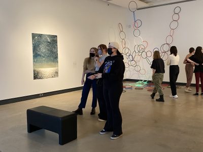 8 gallery viewers in front of art installation of painting and large coloured hoops hanging from ceiling