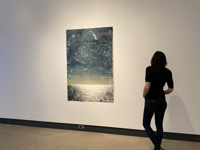 a woman looks at a large abstract painting of an ocean scene at night hanging on wall