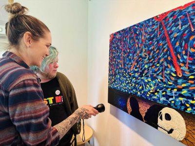 Willow community artists view a message written in invisible ink at the bottom of a painting.