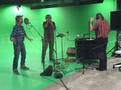 2 performers and a sound tech in front of green screen in the media room