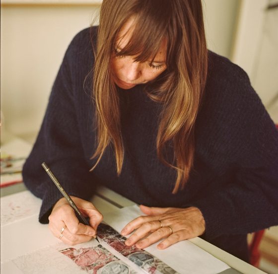 Photo of Claire Greenshaw drawing at a desk.
