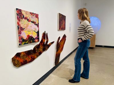 A student observes paintings, including two in the shape of hands, in the VISA gallery.