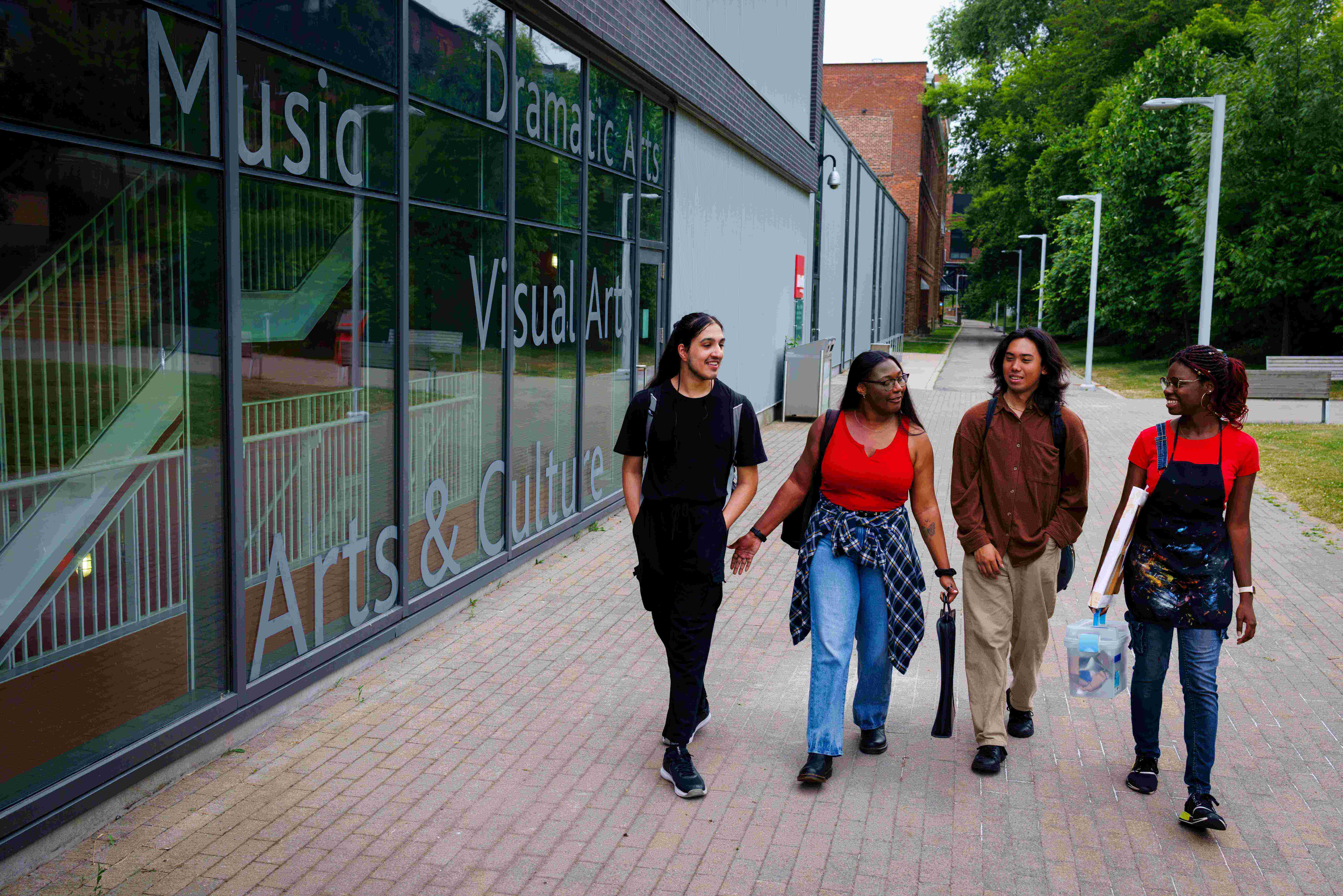 4 students walk and talk behind the Marilyn I. Walker School of Fine and Performing Arts. 