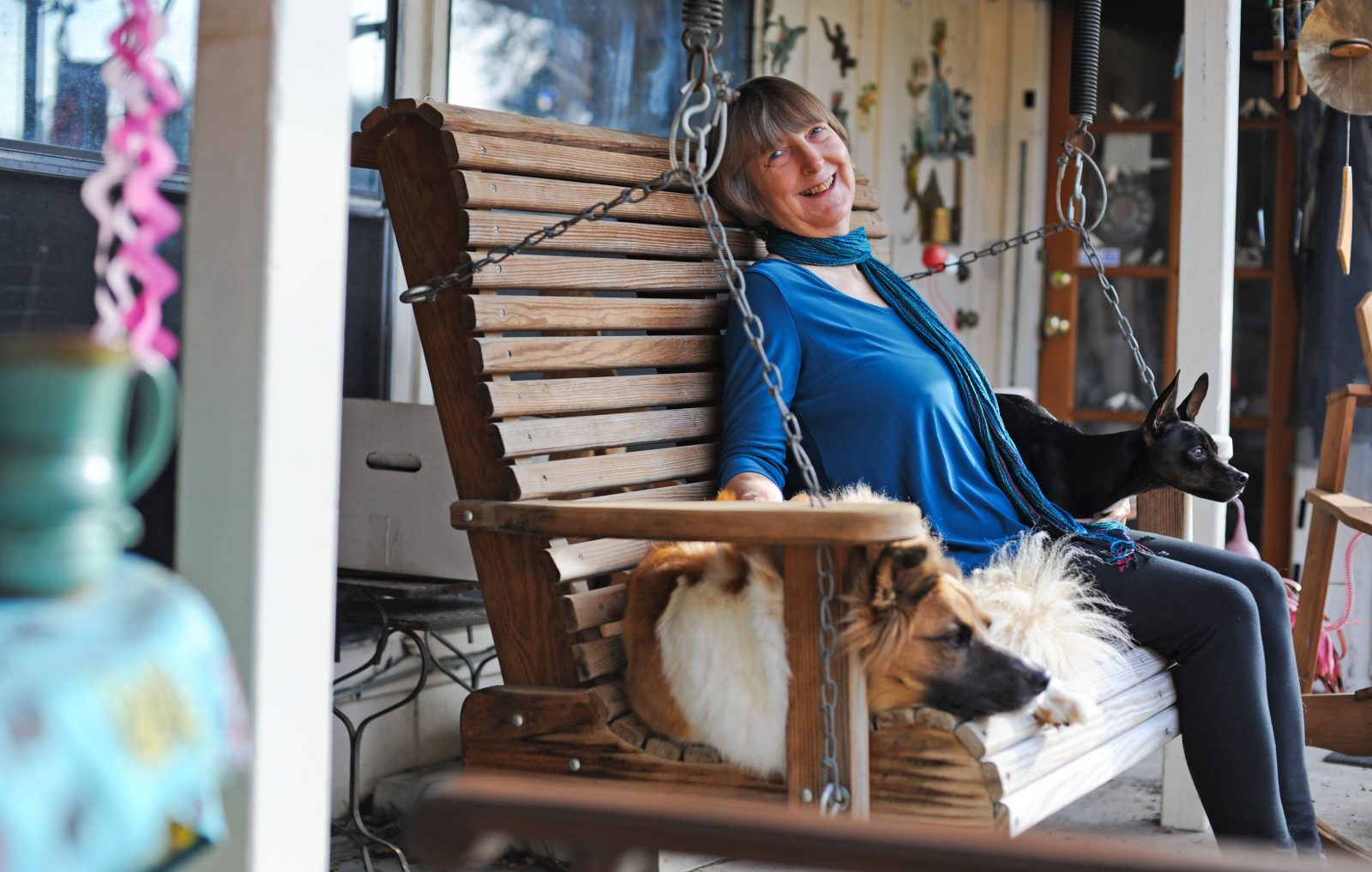 Carol is sat on a porch swing sitting next to two dogs