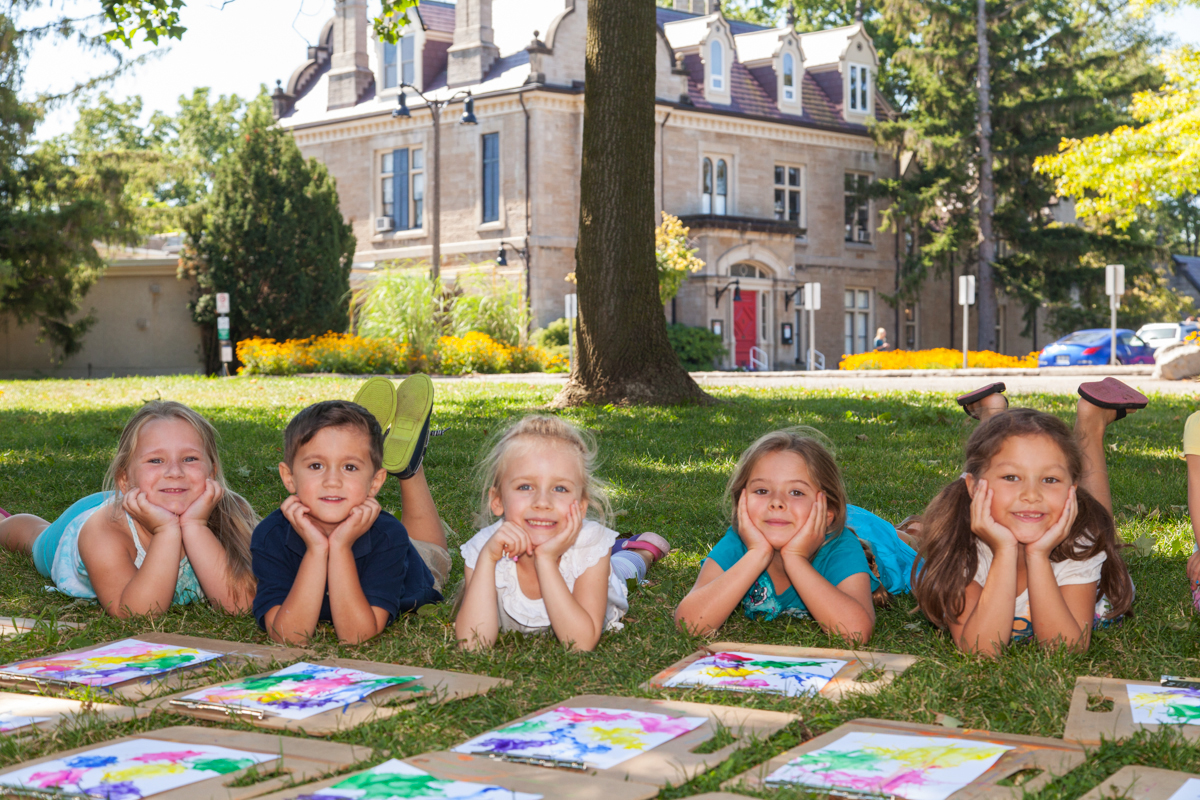 5 yound people laying on grass in front of building with artwork