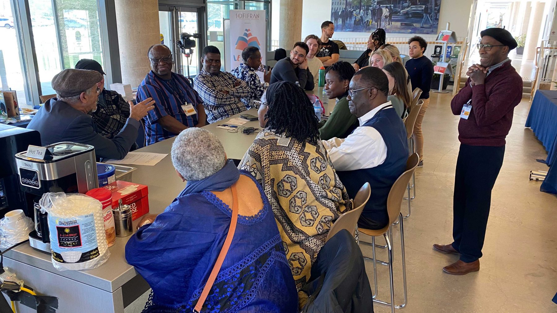 A group of people sit a long table in the MIWSFPA lobby engaged in Discussion.