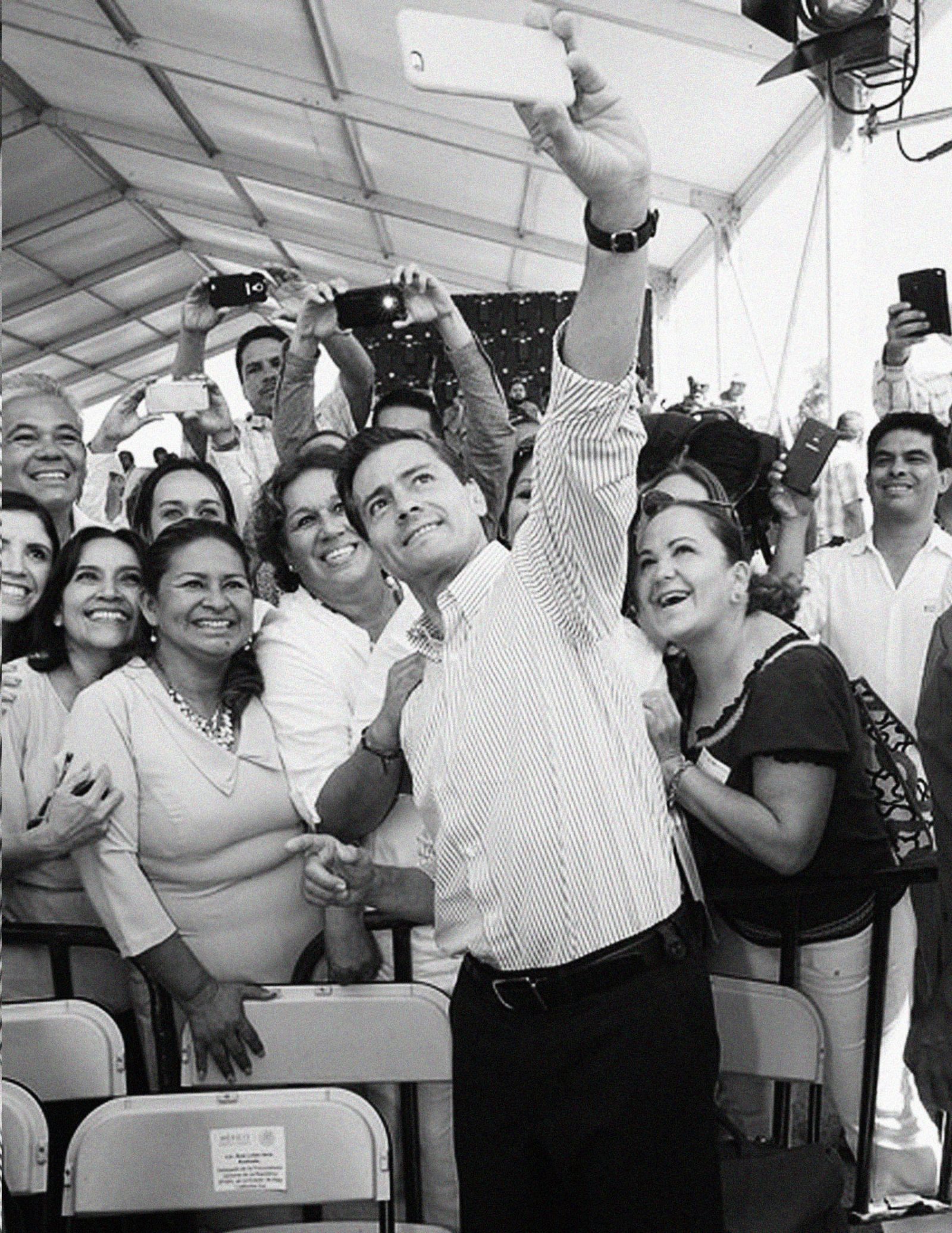 man taking a selfie in front of a group of people in black and white