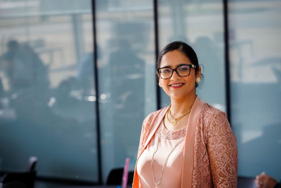 Divya smiles wearing glasses and a nice pink top