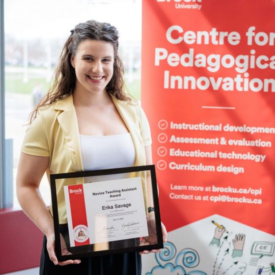 Erika Savage smiles widely holding her Novice TA Award in front of the CPI banner